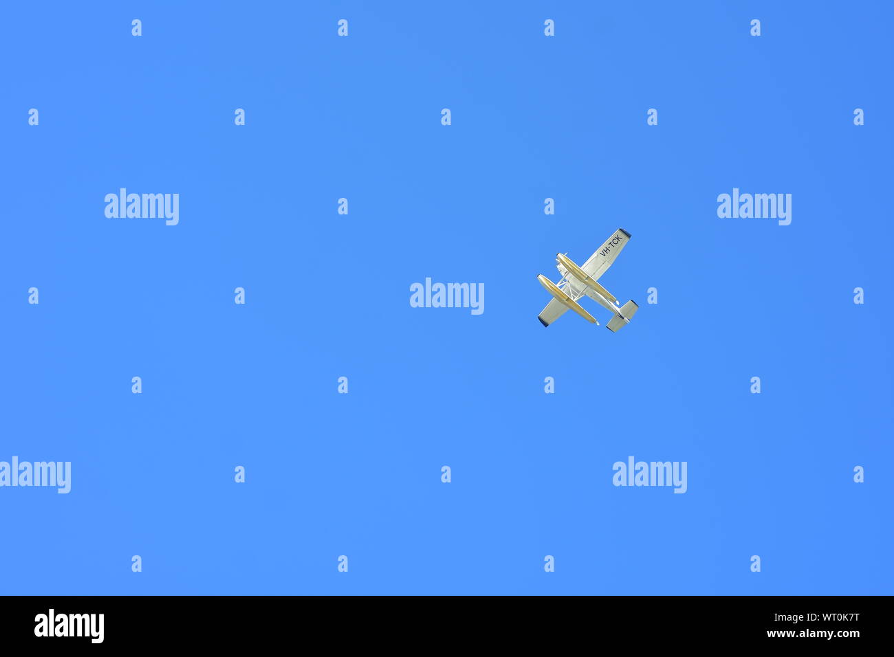 Distante bianco piccolo aereo con galleggianti sotto fusoliera in condizioni di luce solare intensa contro il cielo blu. Foto Stock