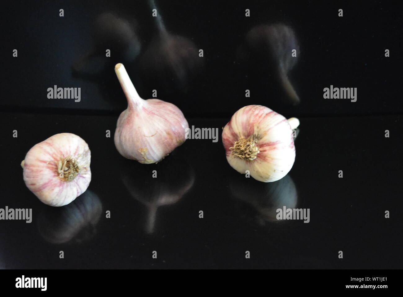 Verdure fresche, tre teste di vitello adagiate su una superficie nera lucida con riflessi ripetuti. Foto Stock