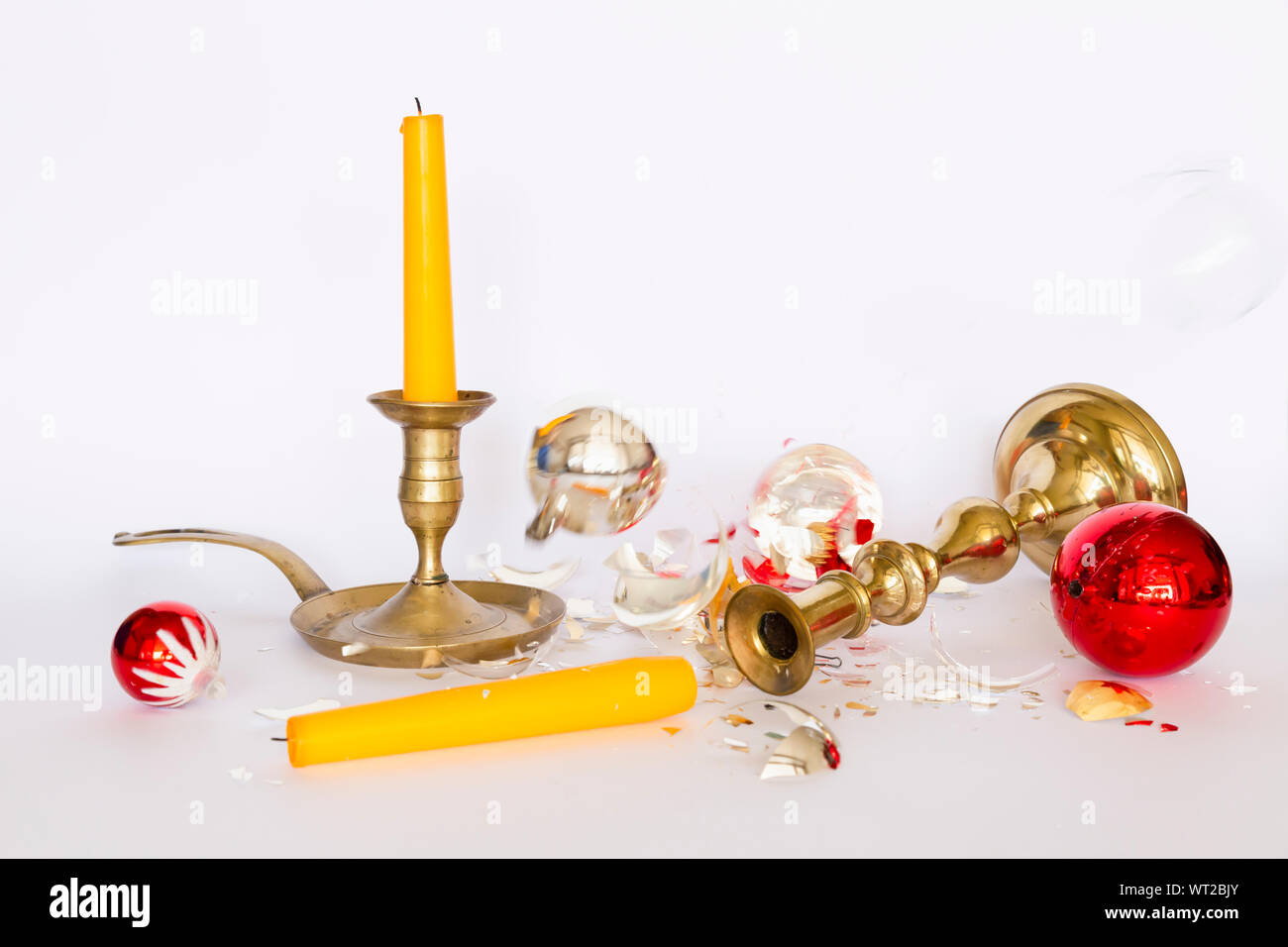 Vista frontale di caduta e frantumato rosso e argento baubles di Natale e due di bronzo portacandele con una candela di colore giallo su sfondo bianco Foto Stock