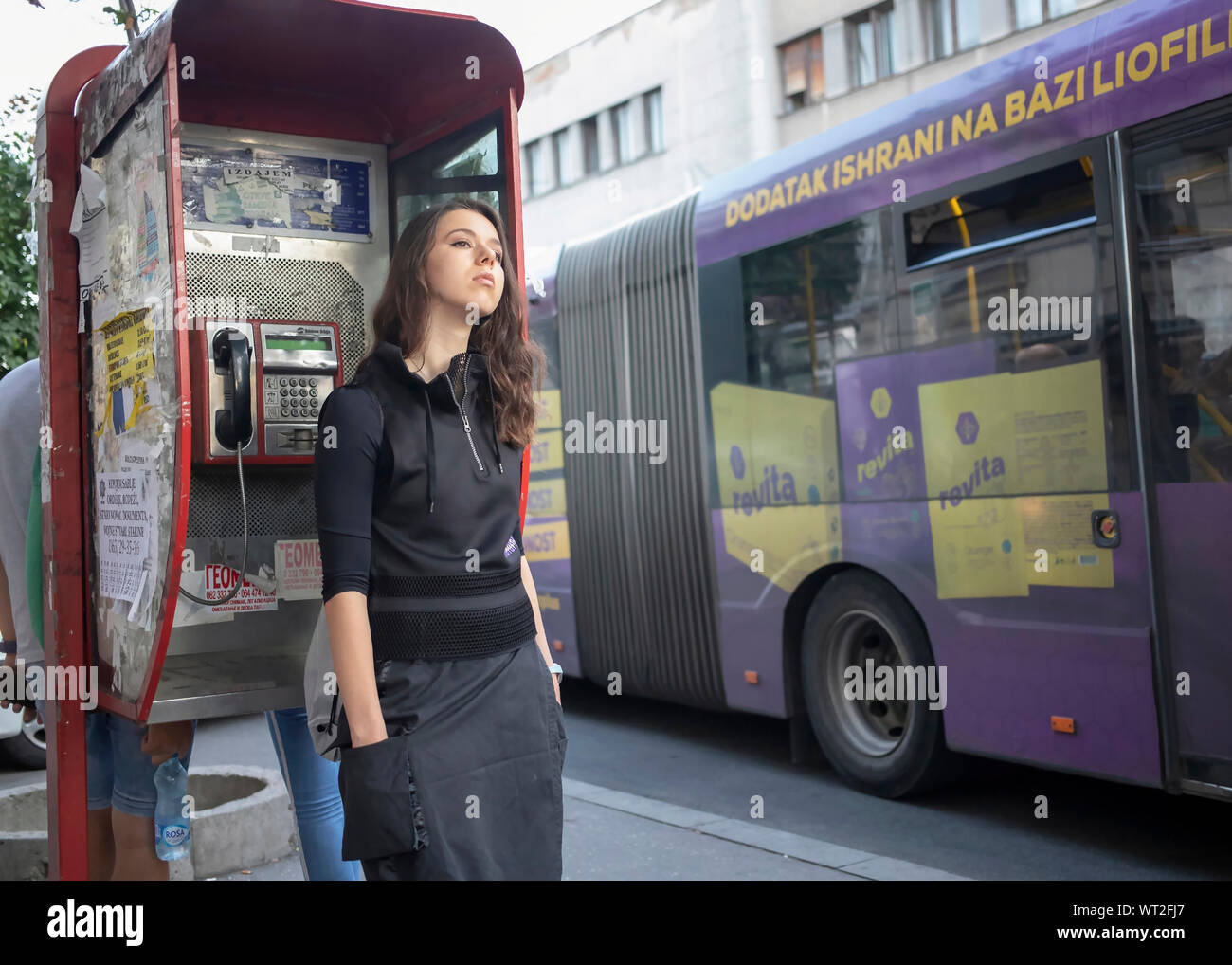 A Belgrado, in Serbia, 10 Settembre 2019: giovane donna in piedi sul marciapiede appoggiato a un telefono a pagamento a Glavna Street a Zemun Foto Stock