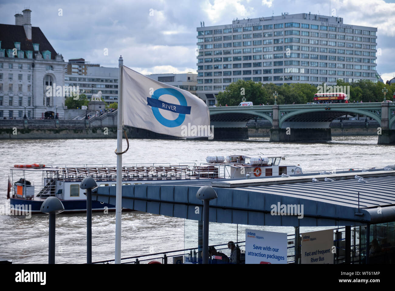 Trasporto fluviale battenti bandiera sulle banchine del fiume Tamigi, con ponte e di costruire in background in London , REGNO UNITO. Foto Stock