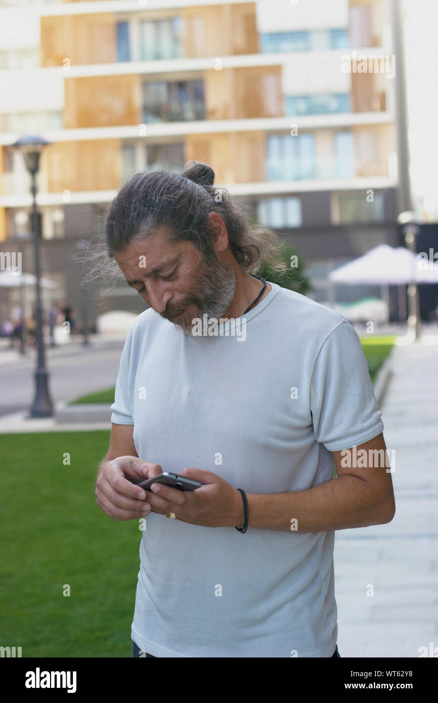 Uomo di mezza età in piedi sulla strada, controllando il suo smartphone Foto Stock