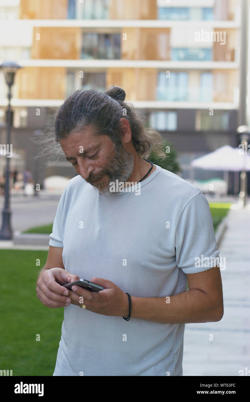 Uomo di mezza età in piedi sulla strada, controllando il suo smartphone Foto Stock