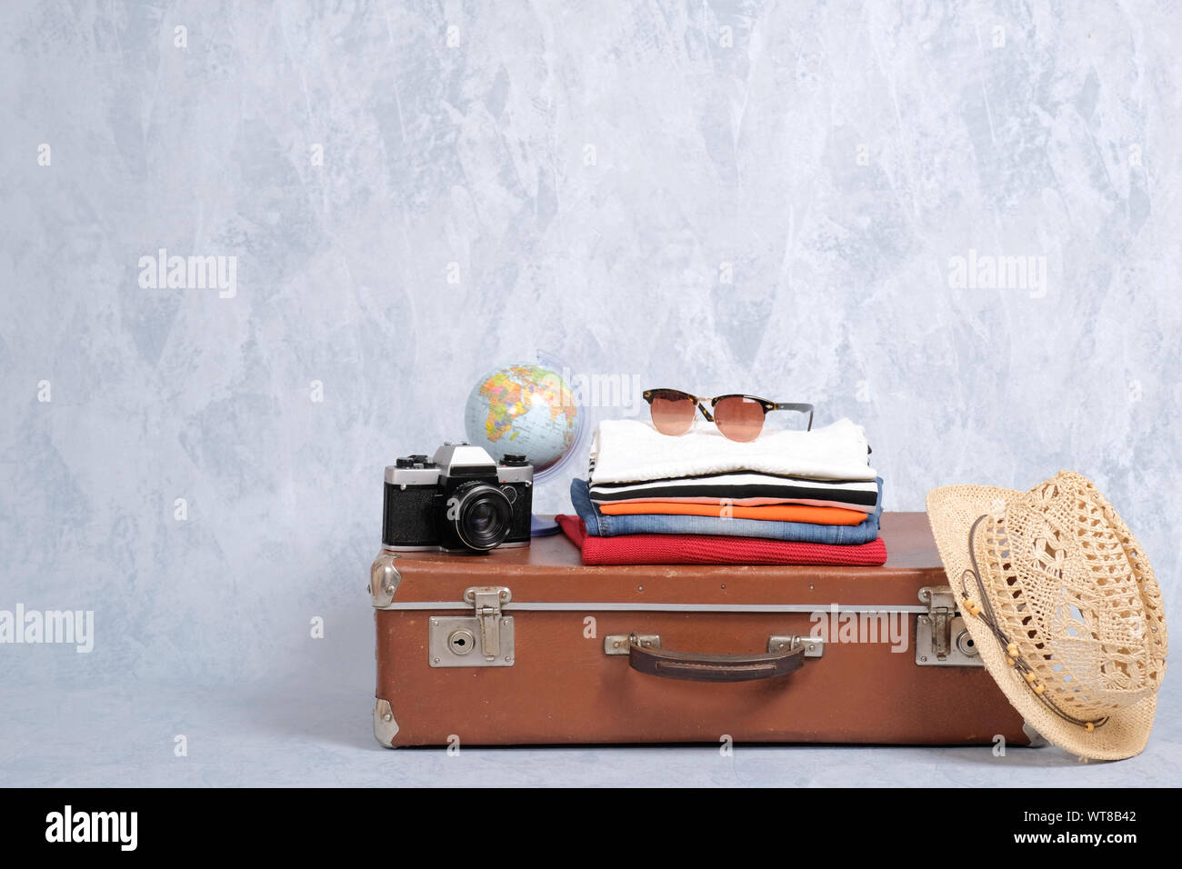 Vecchia valigia viaggio con estate accessori: occhiali, confezione di capi di abbigliamento, retrò fotocamera, spiaggia di paglia hat su sfondo grigio. Banner mocku Foto Stock