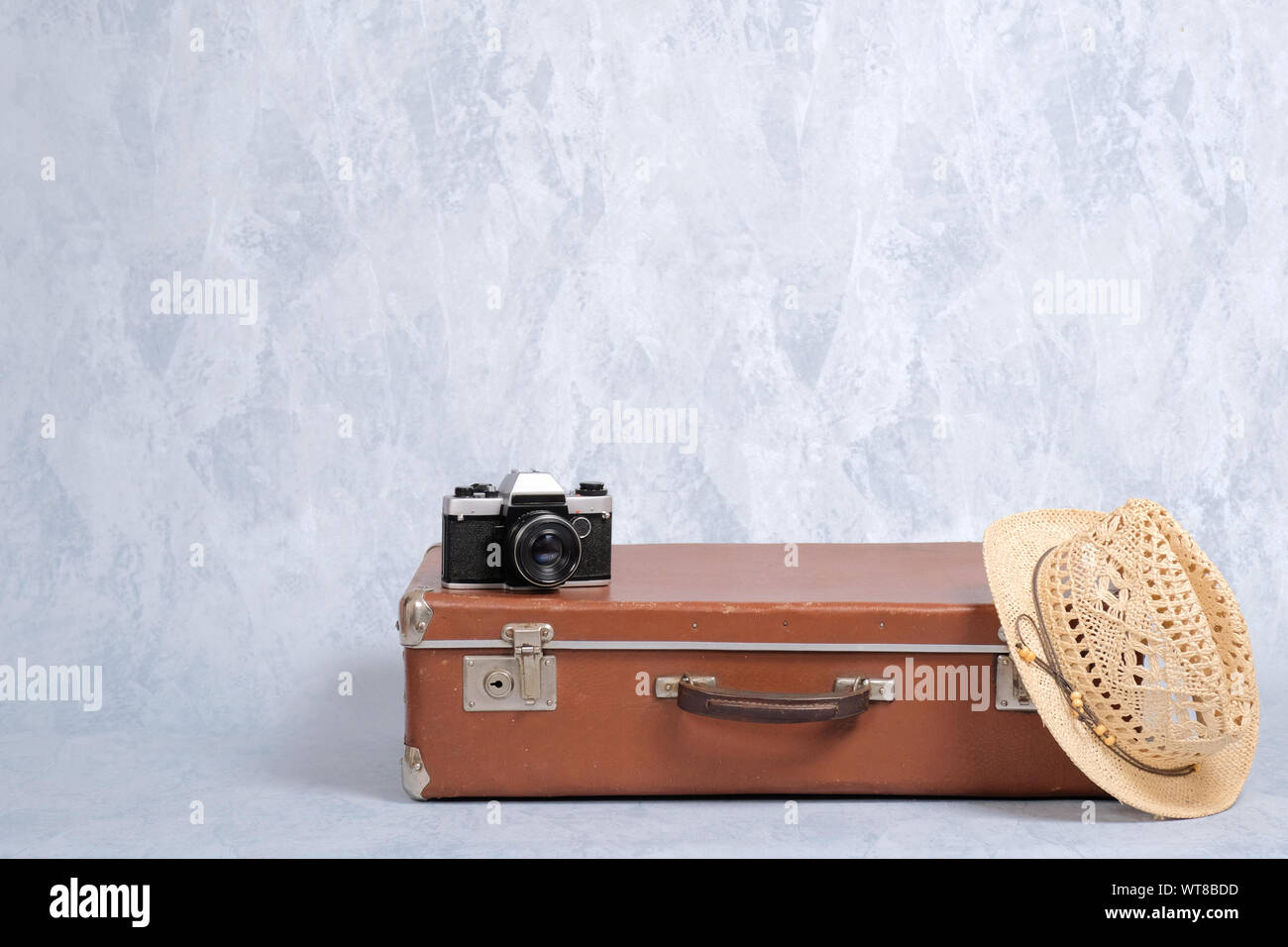 Viaggiare bagaglio a mano vecchia valigia, cappello di paglia, fotocamera a pellicola su sfondo grigio. Concetto di viaggiare con riporto su bagagli, elegante travel, j Foto Stock
