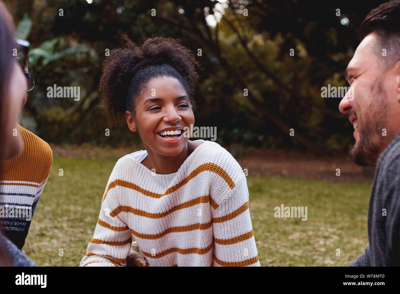 Ritratto di un sorridente giovane donna africana seduto e godendo con i suoi amici nel parco Foto Stock