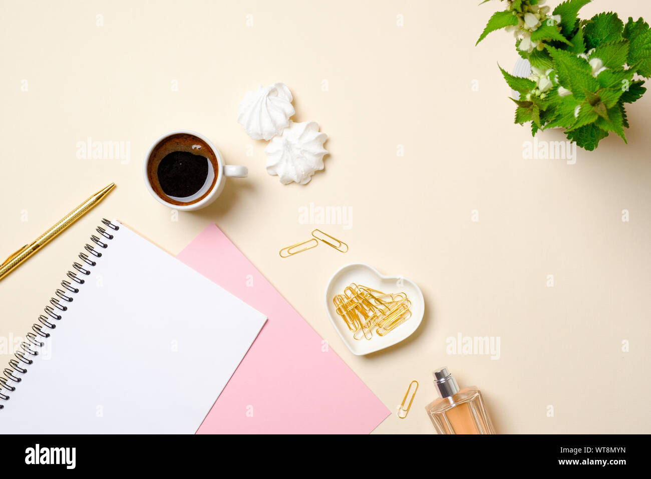 Appartamento laici accessori femminili, carta bianca notepad, tazza di caffè, marshmallow, bottiglia di profumo, fiori sui colori pastello sfondo beige. Vista superiore beaut Foto Stock