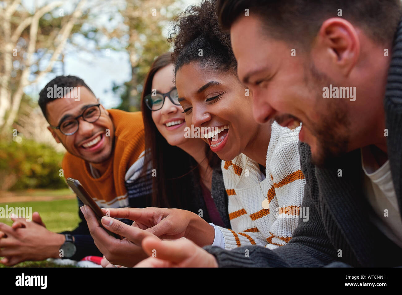 Gruppo di multi etnico amici in college giacente insieme nel parco godendo la visione di testo o video sul telefono cellulare - gruppo sorridente degli studenti Foto Stock