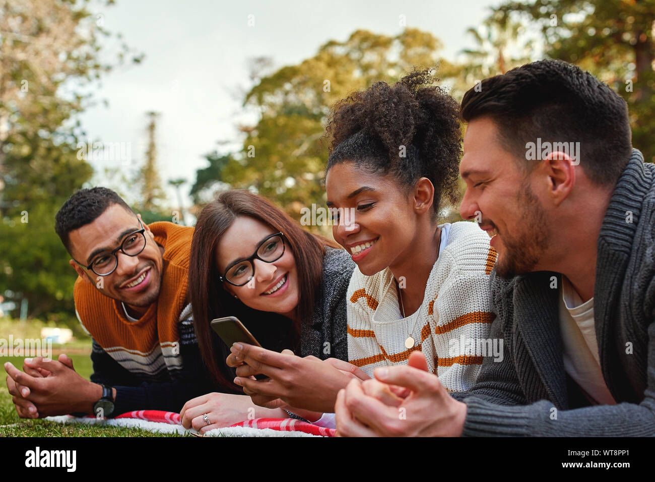 Gruppo di felice diversi amici guardando americano africano donna utilizzando il suo telefono cellulare nel parco su una giornata d'estate - molto felice giovane gruppo di Foto Stock