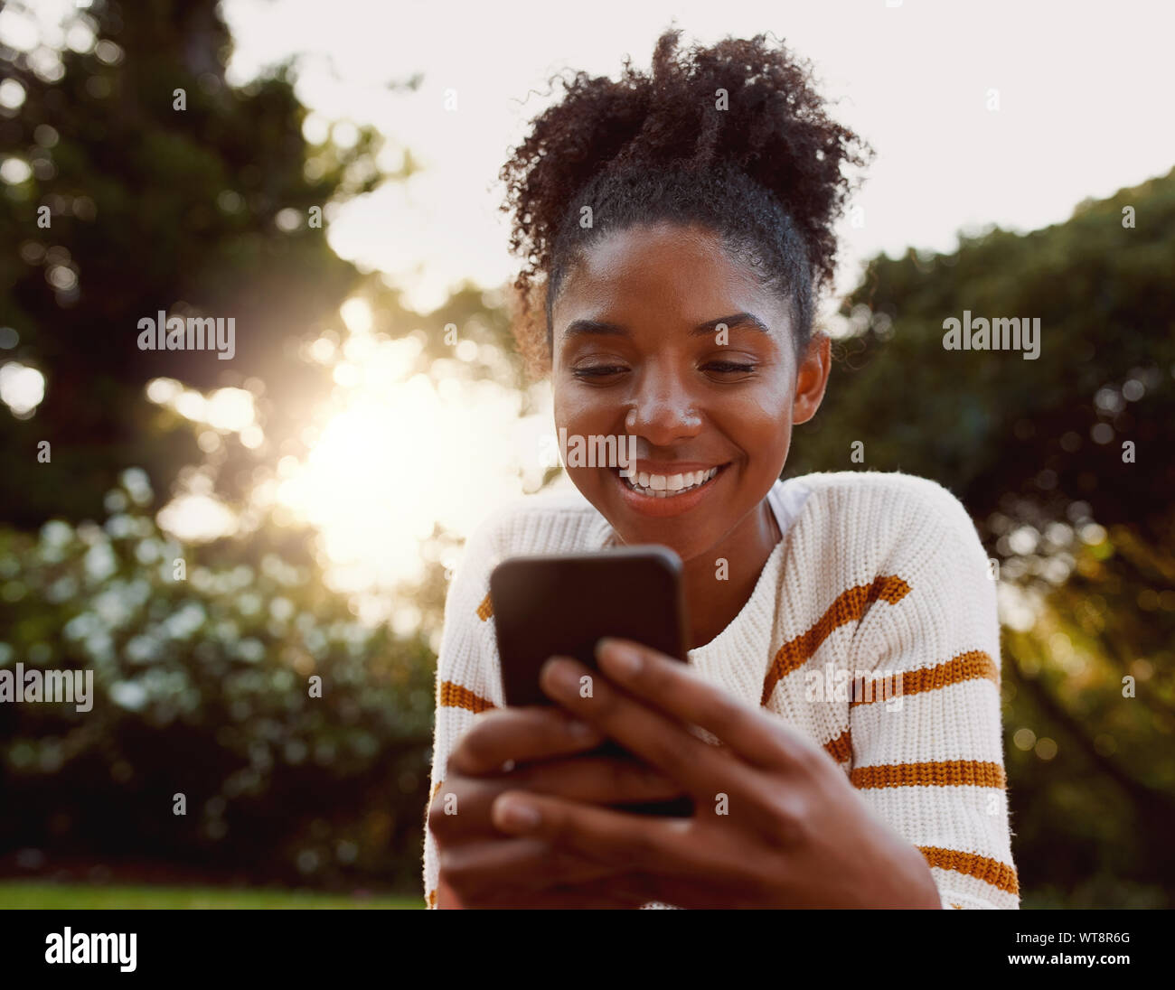 Ritratto di un americano africano giovane donna utilizzando il telefono cellulare nel parco sulla giornata di sole sorridenti - Molto donna felice sul cellulare Foto Stock