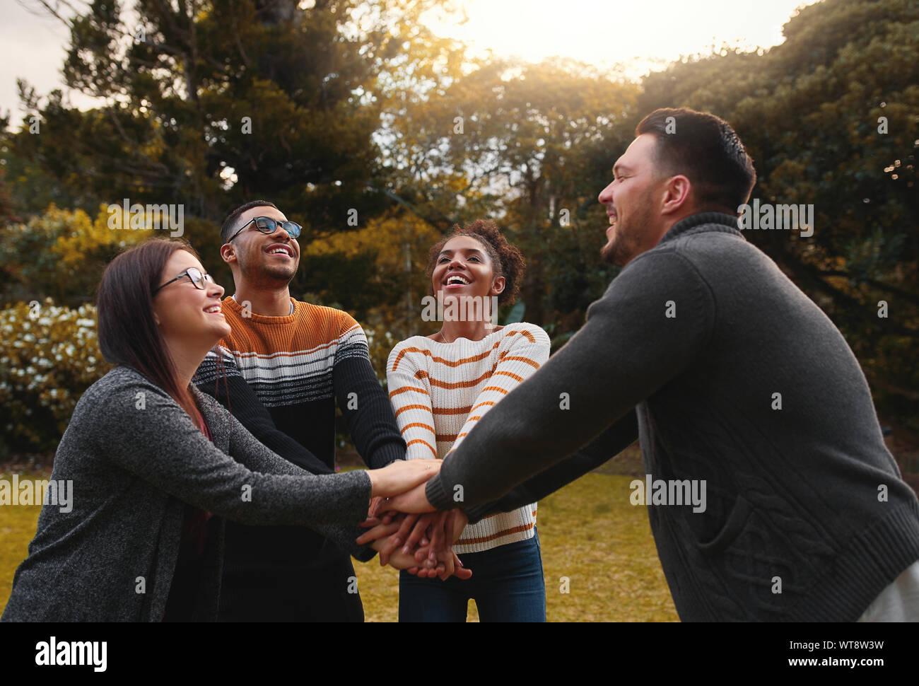 Gruppo di felice amici multietnica insieme in piedi in cerchio in corrispondenza di impilamento del parco le loro mani Foto Stock