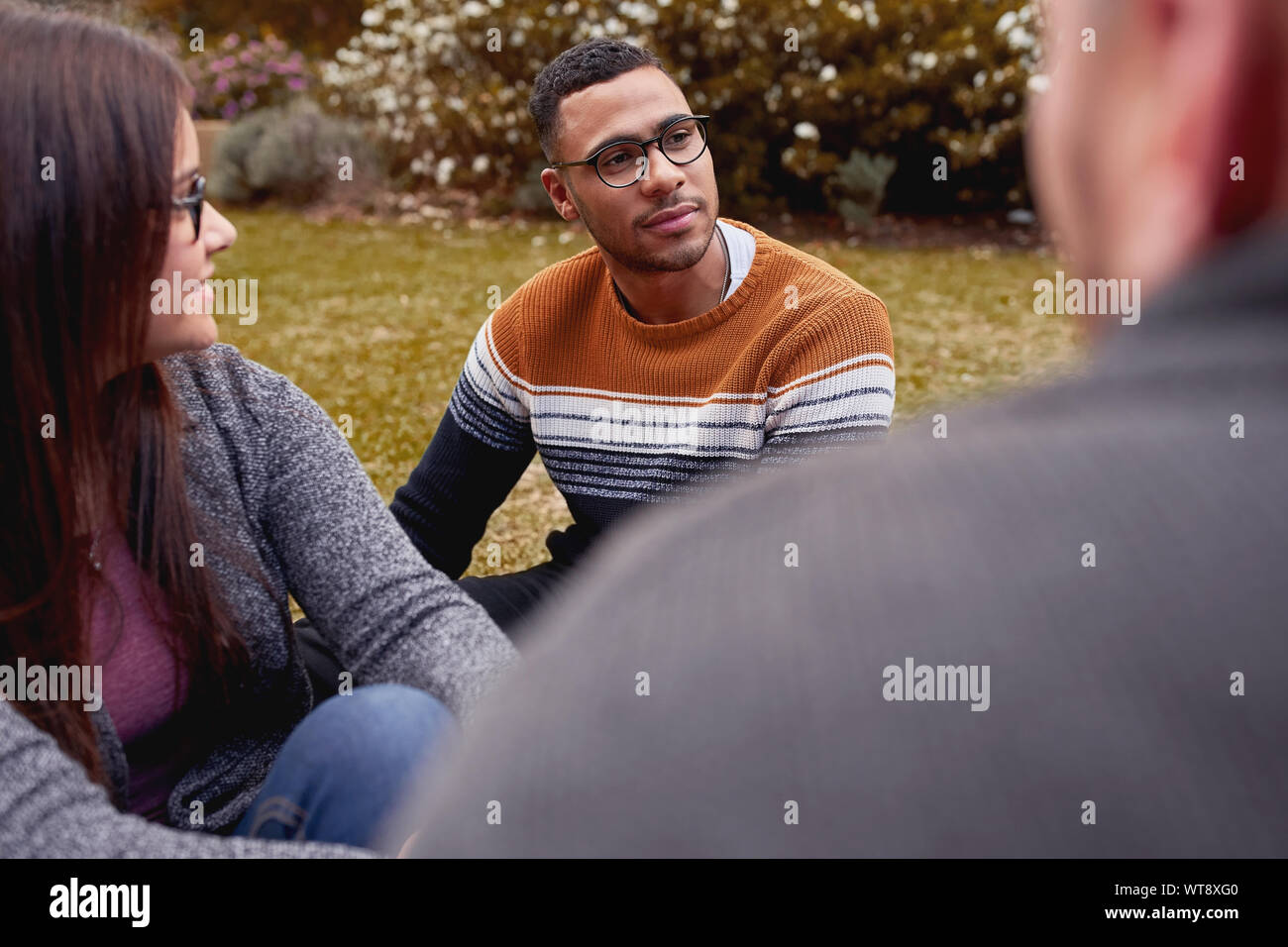 Bel giovane africano seduti insieme con gli amici e multirazziale nel parco Foto Stock