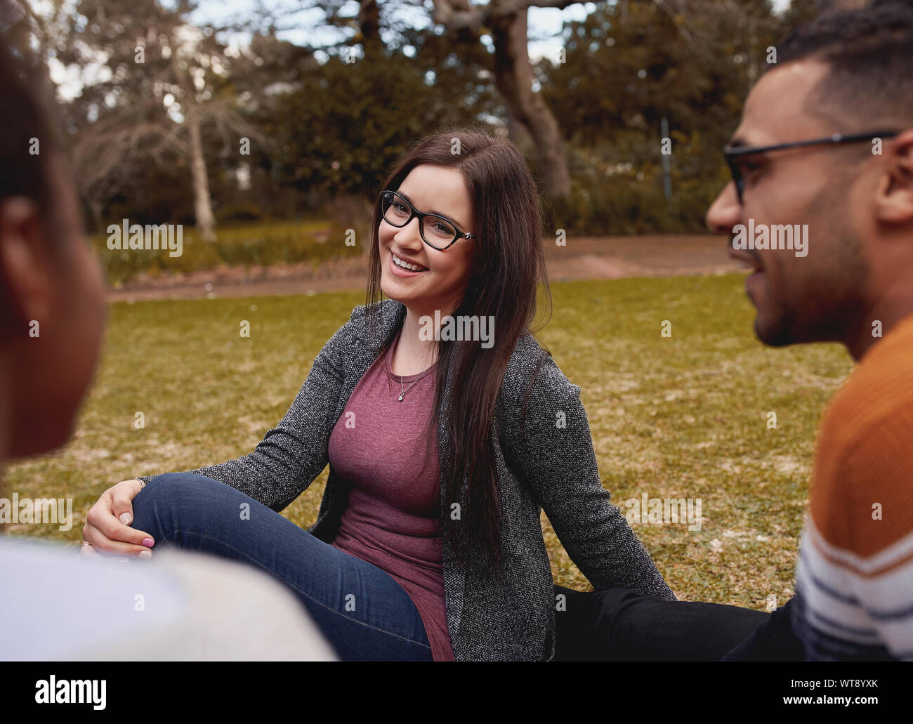 Ritratto di una bella sorridente giovane donna indossa occhiali rilassante con il suo amico nel parco Foto Stock