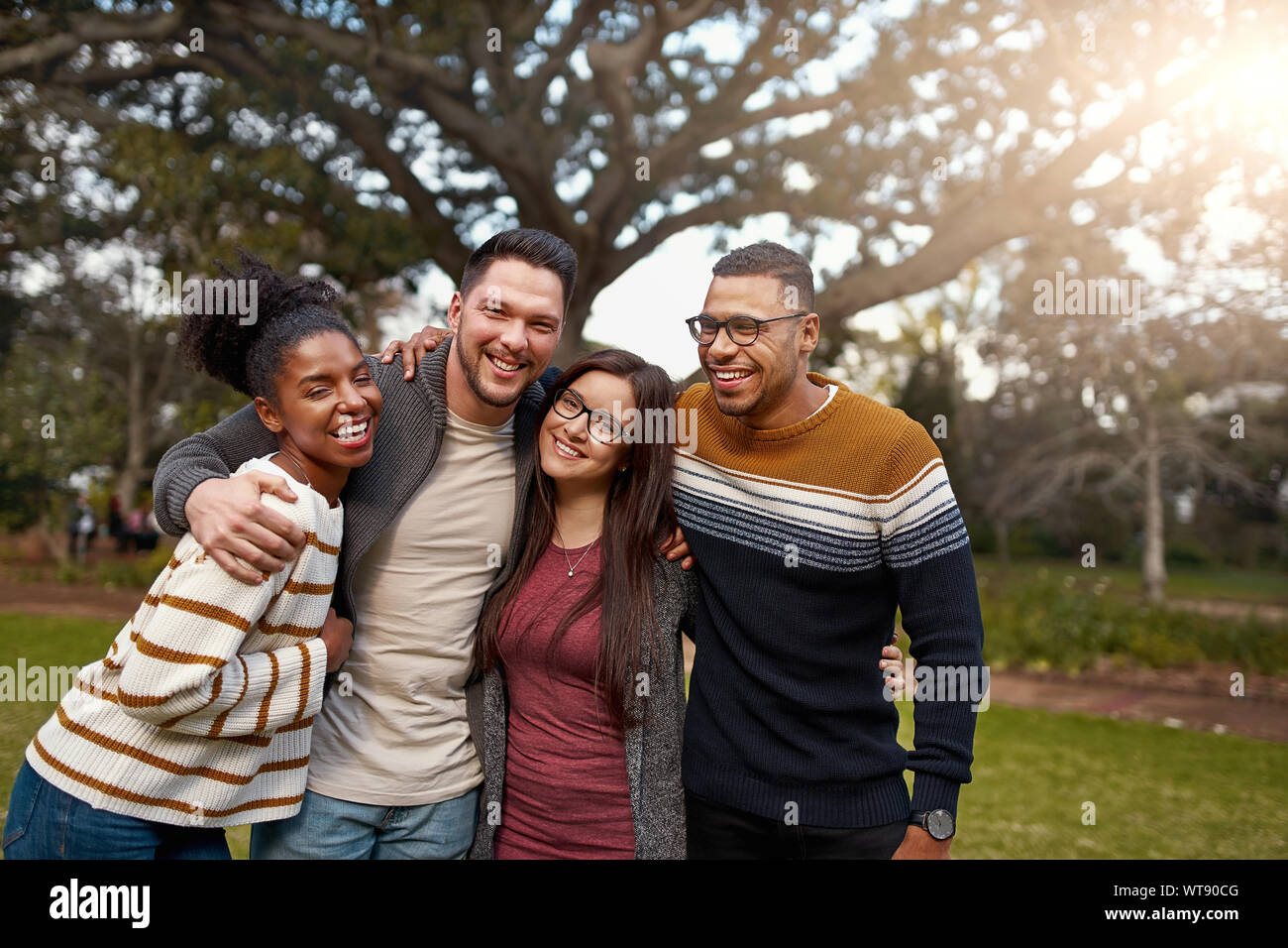 Sorridente gruppo di amici a ridere insieme mentre in piedi con le braccia intorno a ogni altro a un parco - happy gruppo di persone Foto Stock