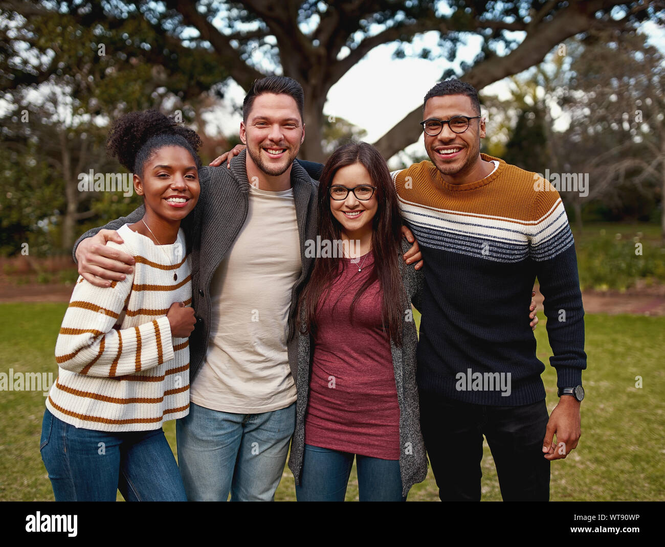 Ritratto di un sorridente variegato gruppo di giovani amici in piedi insieme al parco all'aperto in una giornata di sole Foto Stock