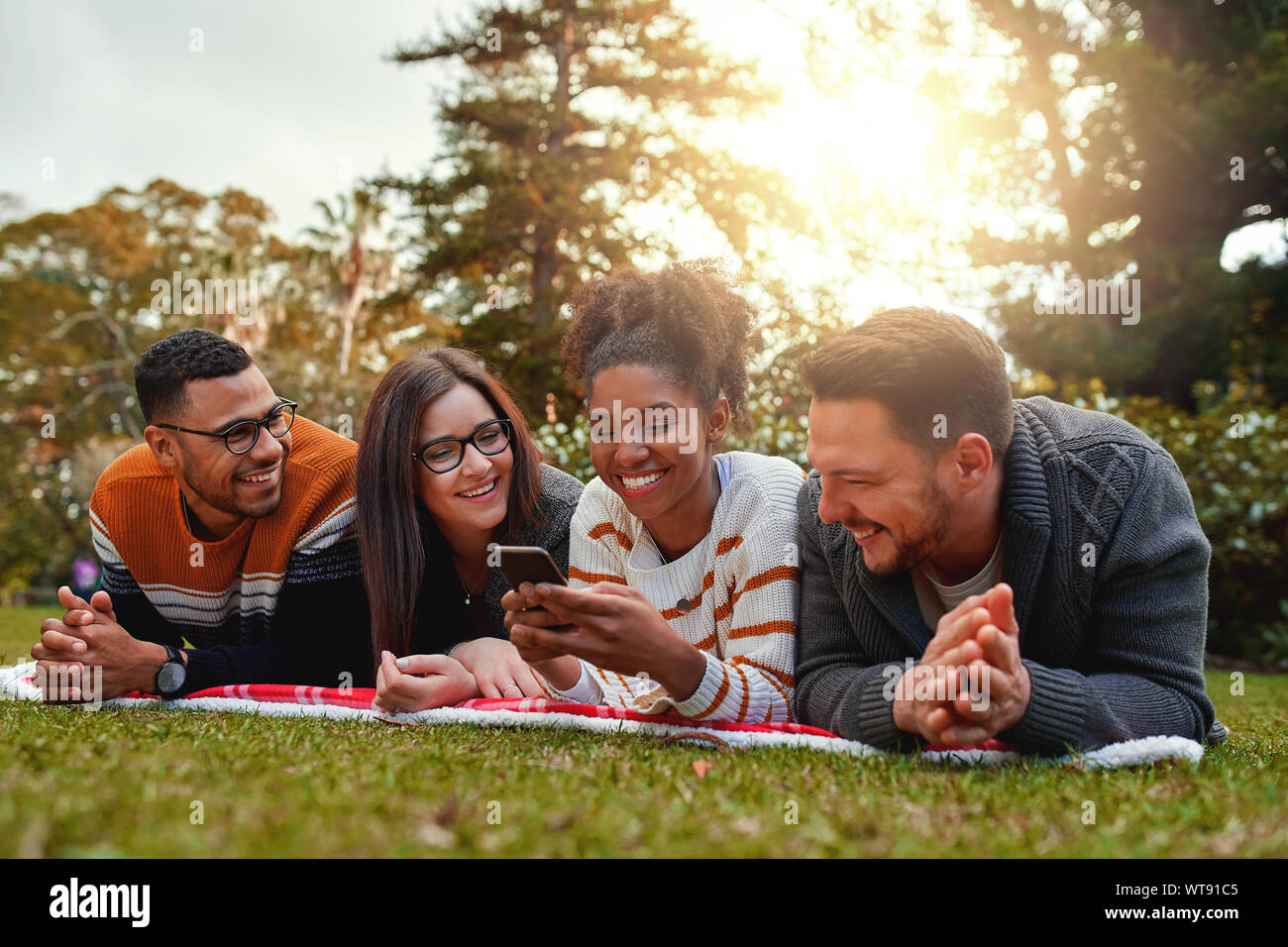 Sorridente americano africano donna sdraiata con il suo gruppo multietnico di amici gli sms su un cellulare in un parco - molto felice gruppo di amici Foto Stock