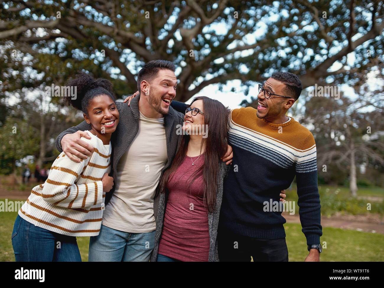 Diversi gruppi di giovani felici amici americani insieme in piedi nella parte anteriore della struttura ad albero park - giovani e divertimento e all'aperto Foto Stock