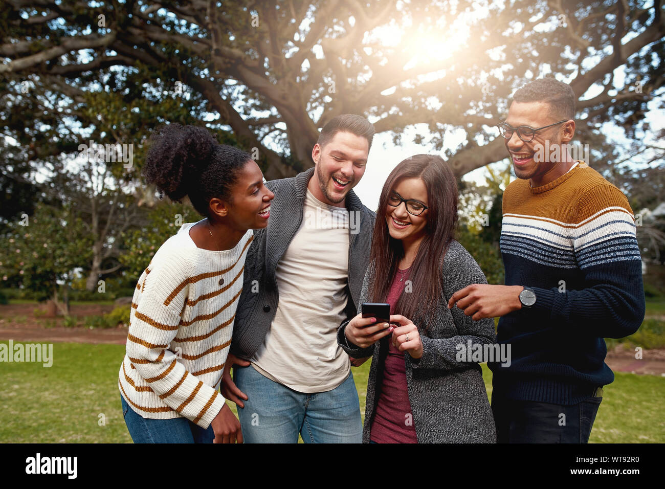Gruppo diversificato di felice amici assieme a ridere e guardando a smart phone nel parco - vestito molto alla moda Foto Stock