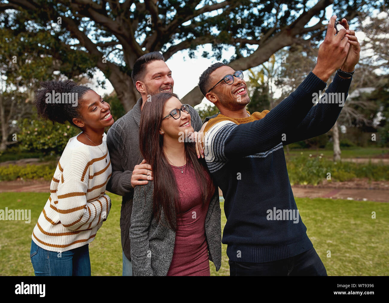 Gruppo di multirazziale giovani amici stando insieme in un parco verde di prendere una selfie sul telefono cellulare sorridenti - un picnic estivo Foto Stock