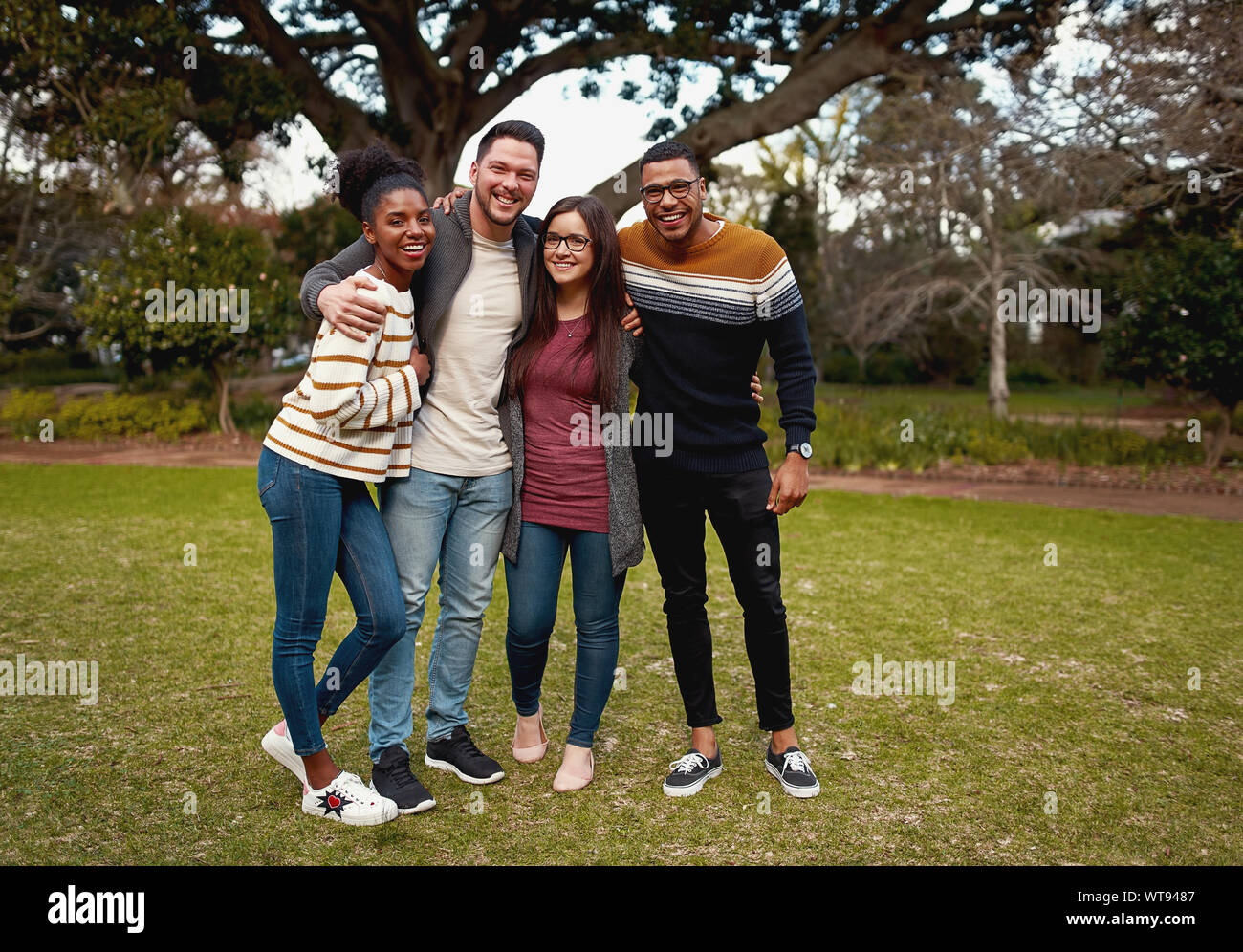 Gruppo sorridente di amici nel quartiere alla moda di abbigliamento casual in piedi insieme nel parco all'aperto sorridente e molto felice - guardando la fotocamera Foto Stock