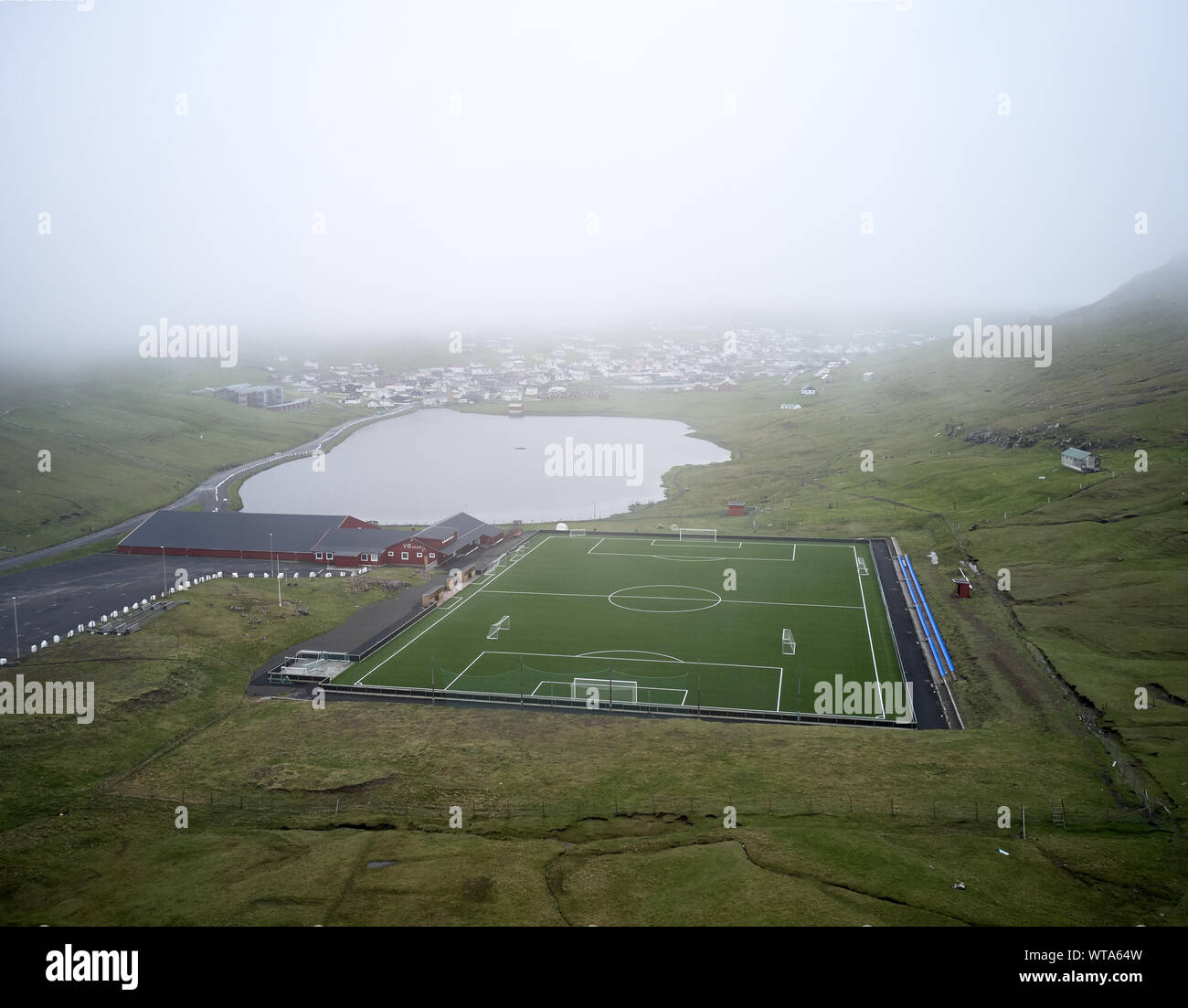 Da sopra lo stadio di grandi dimensioni con marcature bianche poste in verde valle tra le colline in nebbioso giorno nelle isole Faerøer Foto Stock