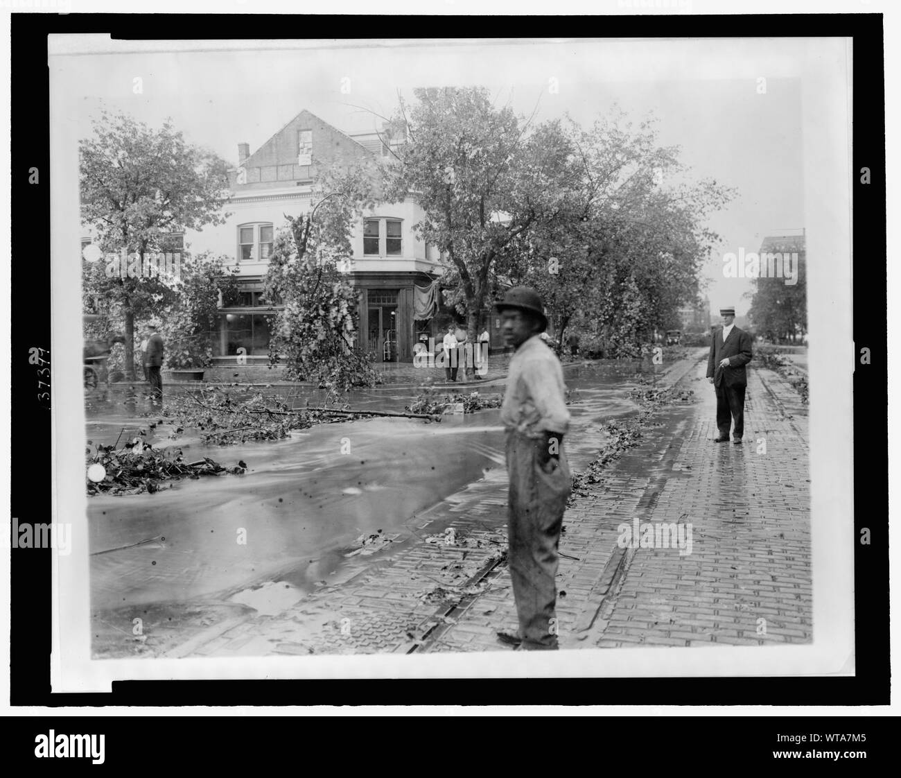 Gli uomini in piedi che guarda a rami di alberi e altri detriti e acqua alta in strada dopo una tempesta Foto Stock