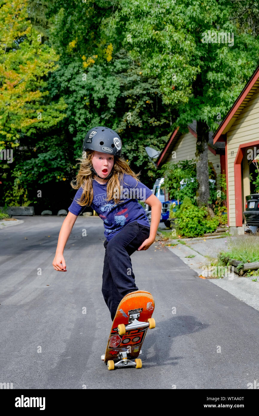 Giovani dai capelli lunghi boy lo skateboard su strada residenziale. Foto Stock