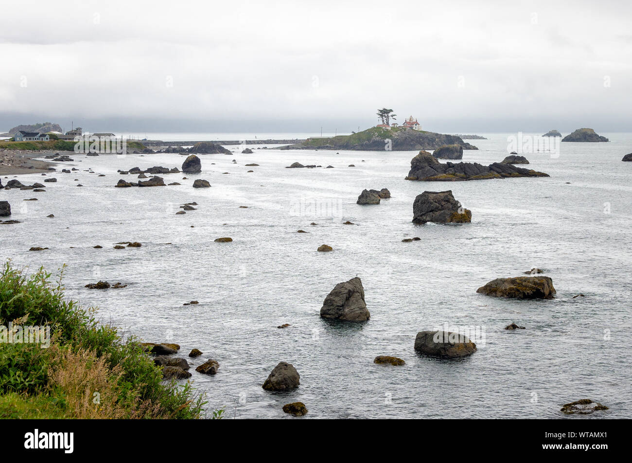 Baia punteggiata di pile di mare e un'isola con un faro lungo la costa della California del Nord in una nebbiosa mattina d'estate Foto Stock