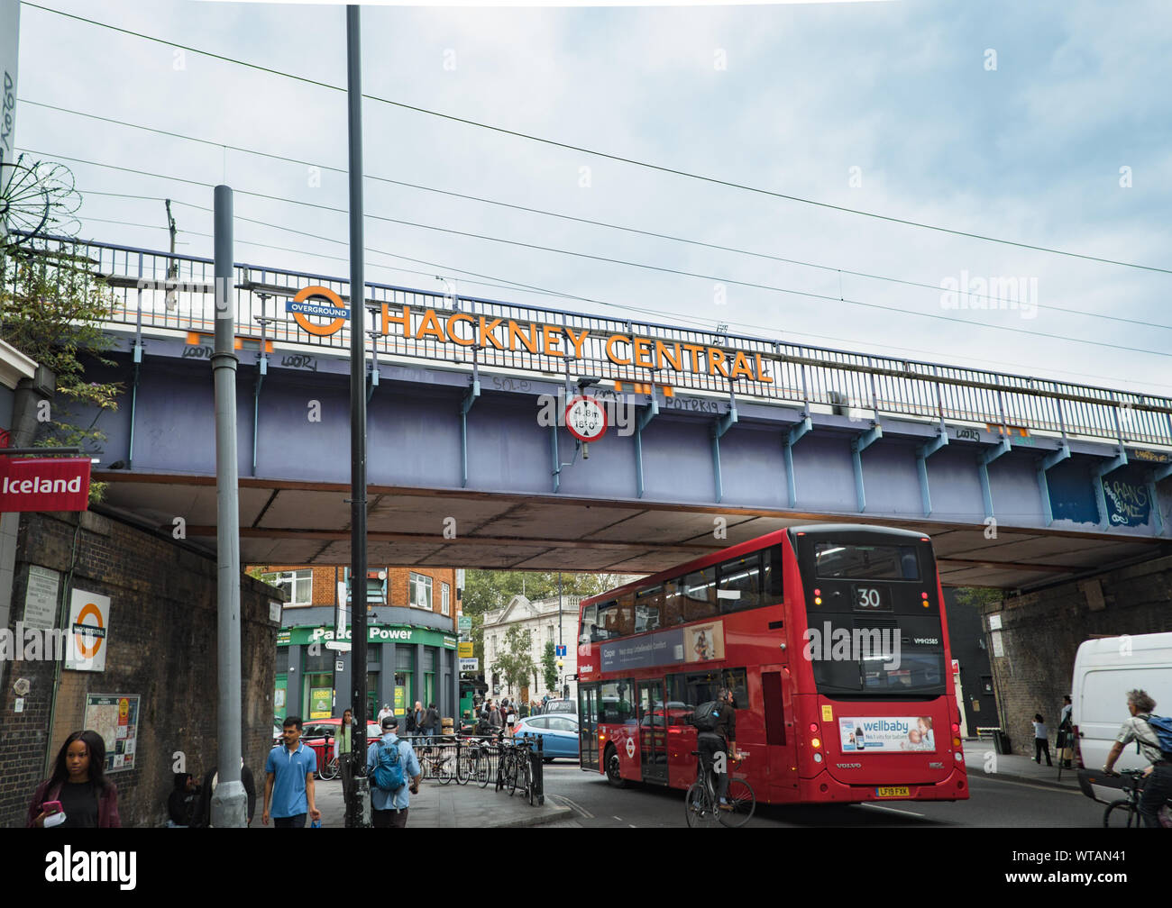 Red London bus passa sotto un ponte ferroviario con segnaletica per centrale di Hackney Overground stazione in mare St, Hackney, a est di Londra, Regno Unito Foto Stock