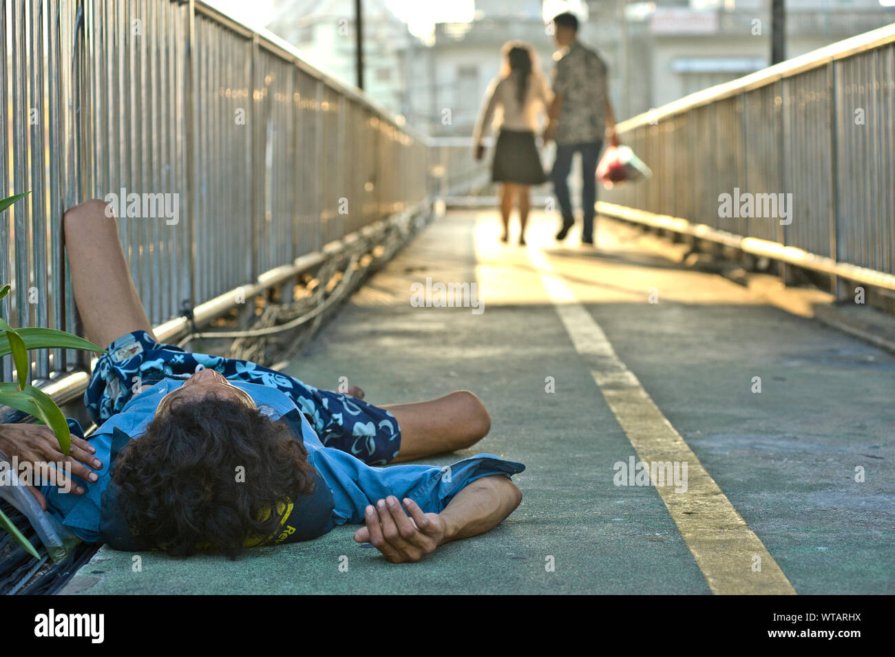 Senzatetto di dormire sulla passerella e giovane a piedi con le mani giunte Foto Stock