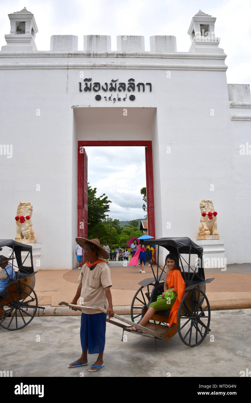 Kanchanaburi, Thailandia, 09.09.2019: bella ragazza Thailandese in stile tradizionale Tailandese, Siamesi abito in un vecchio rickshaw davanti all'ingresso di 'Mallika Cit Foto Stock