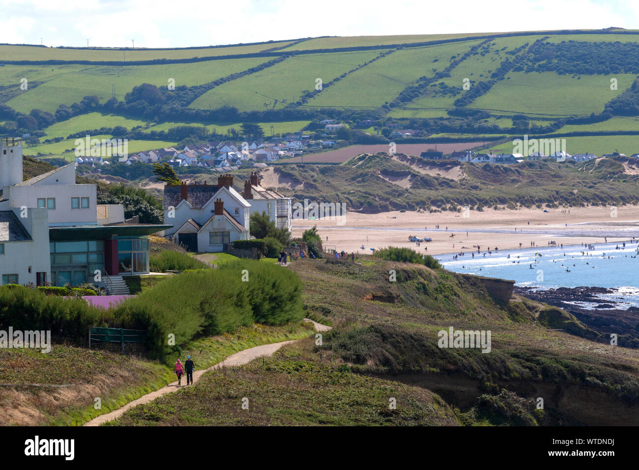 Coppia a piedi lungo il sentiero sopra Croyde Bay e la spiaggia di surf e la città sul mare di Croyde, North Devon, Inghilterra, Regno Unito Foto Stock