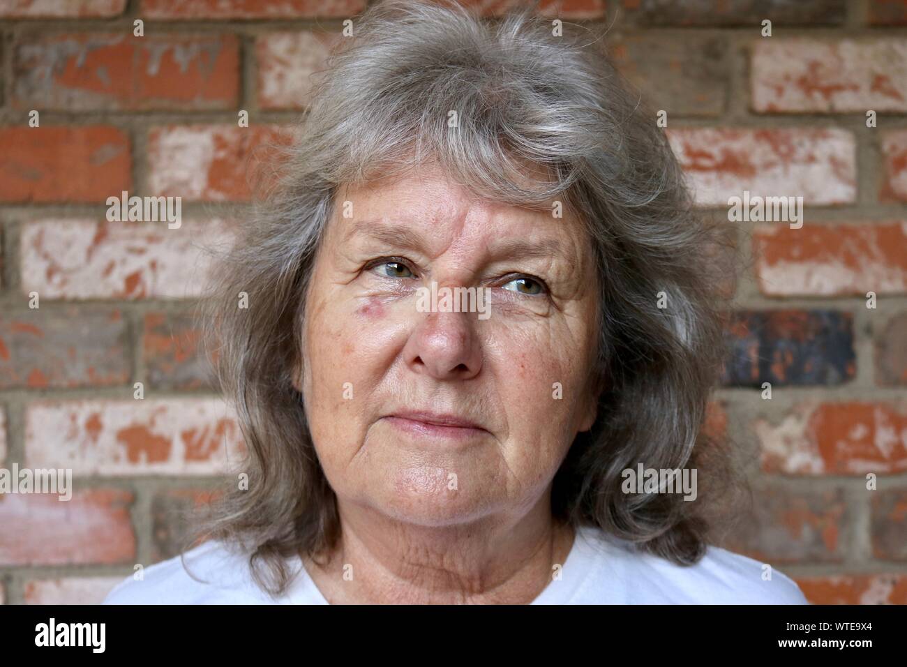 Ritratto di un pelo grigio donna che guarda lontano con il dubbio nei suoi occhi Foto Stock