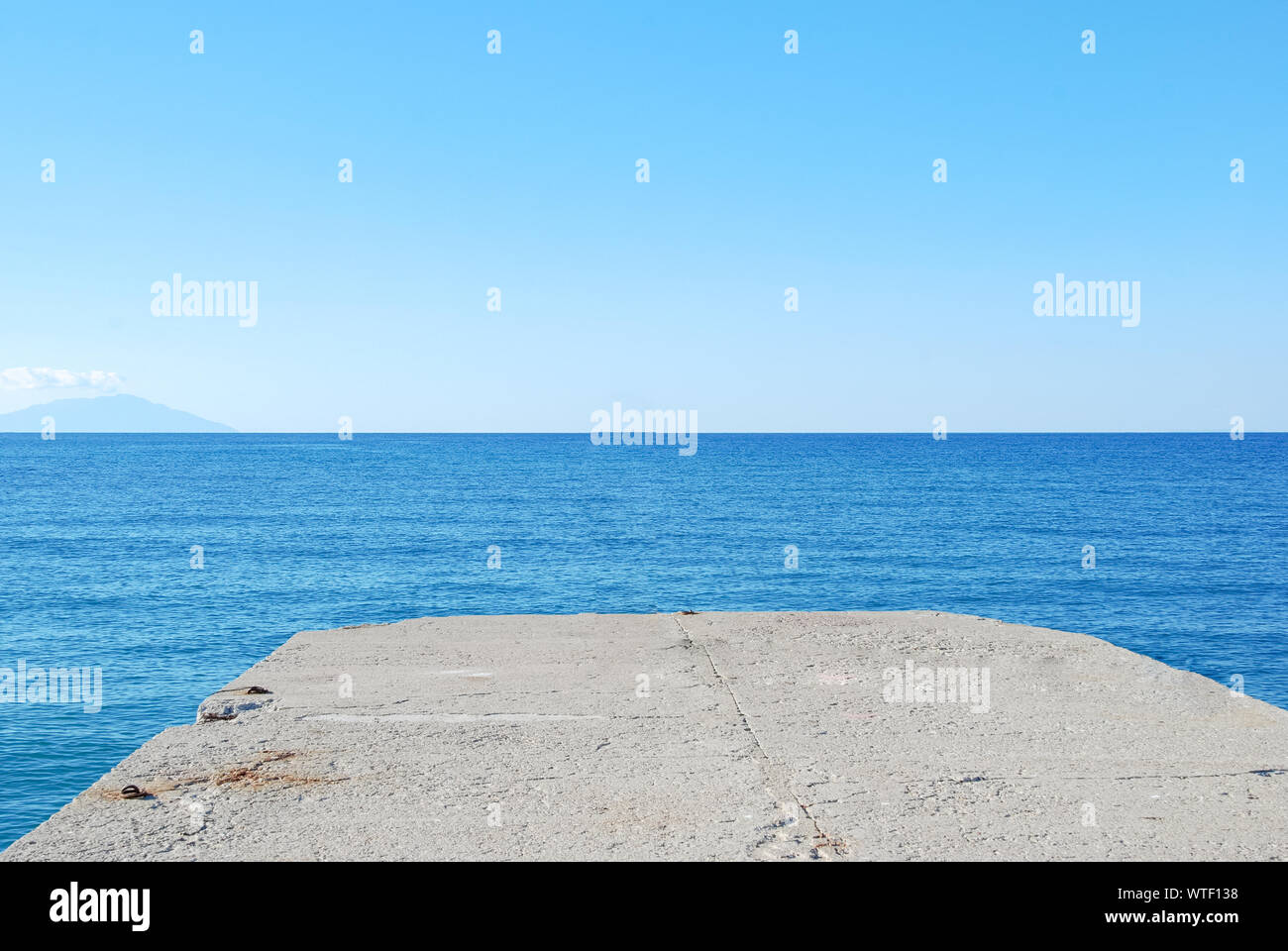 Molo di cemento con un blu mare ondeggiante nel giorno Foto Stock