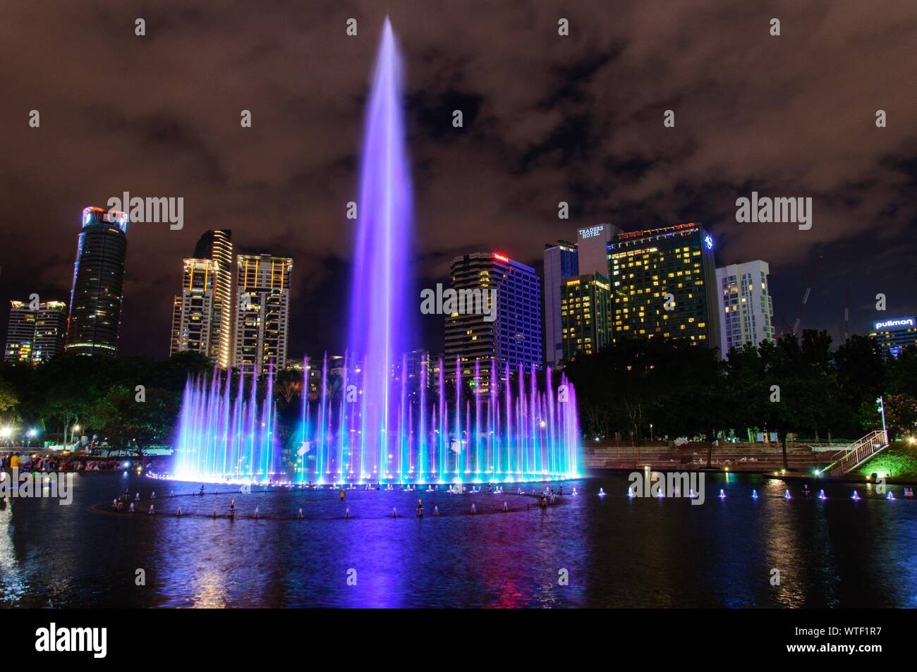 Fontana illuminata a KLCC Park contro il cielo nella città di notte Foto Stock