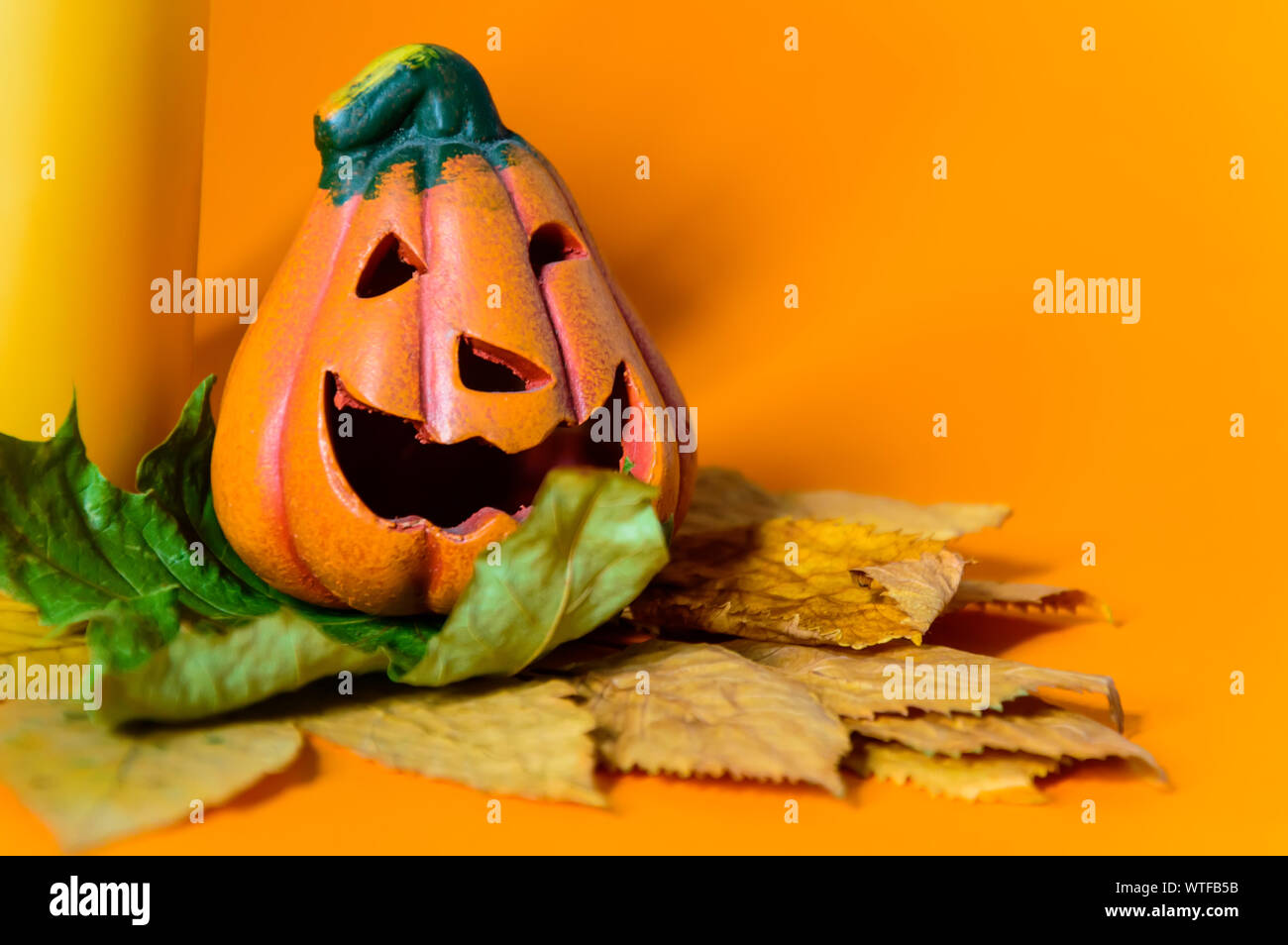 Close-up di ceramica decorativa zucca di Halloween jack-o-lantern sul secco Foglie di autunno e di giallo candela. Foto Stock