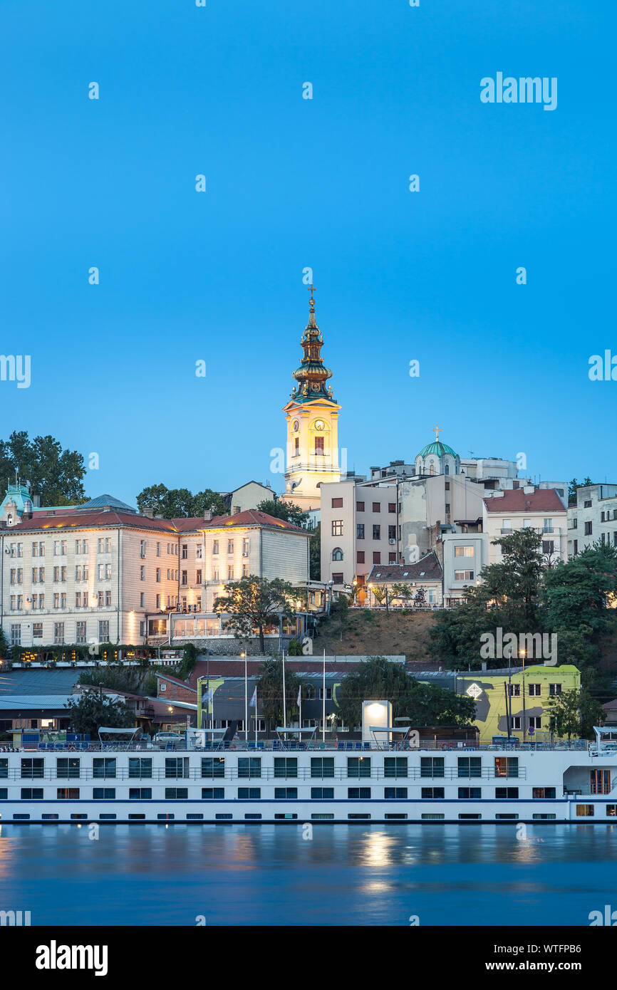 Ora blu vista del lungofiume di Belgrado con il fiume Sava in primo piano, Santo Arcangelo Michele cattedrale sul retro e suggestivo e grande cruiser Foto Stock