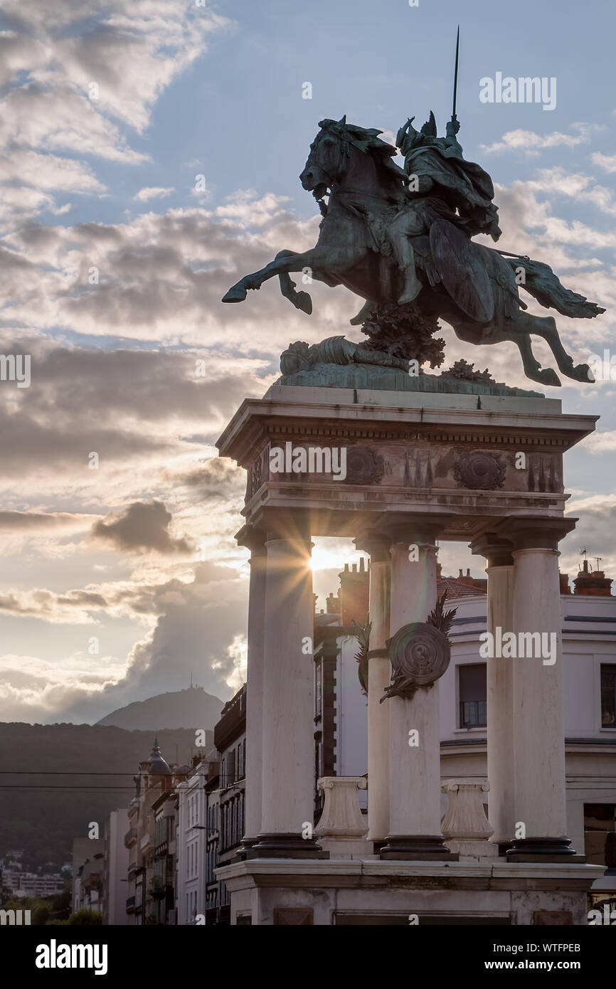 La statua di Vercingetorige su una piazza della città di Clermont Ferrand in Francia, il sole che tramonta e sparare raggi di sole dietro di esso e il Puy de Dome vulcano Foto Stock