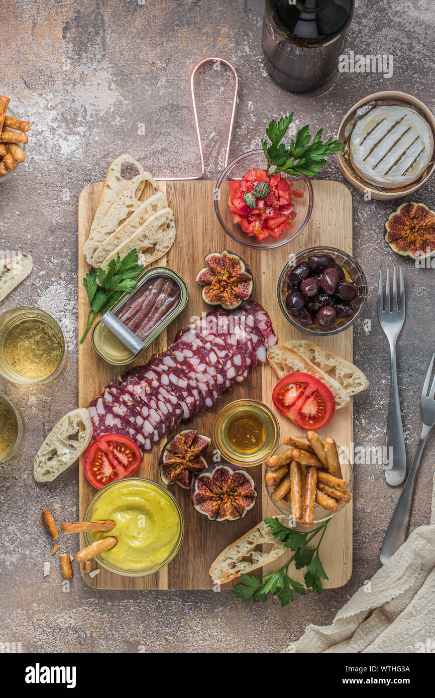 Vino snack set. Bicchiere di vino, selezione di carne, olive, pomodori, baguette a fette, formaggio camembert e spezie tagliere in legno. Foto Stock