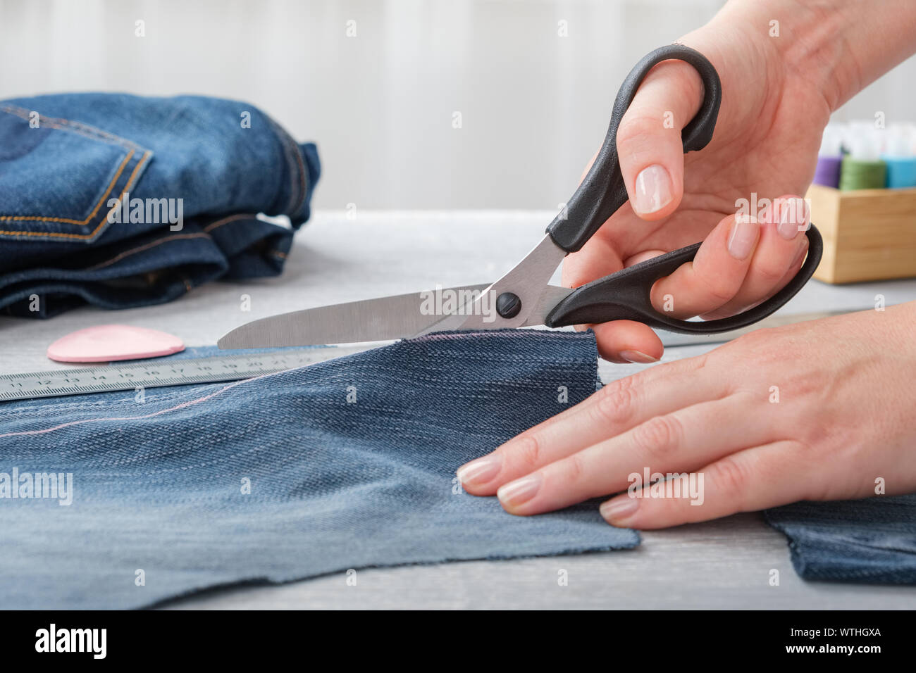 Donna mano che tiene una forbice e il taglio blu jean tessuto sul tavolo. Foto Stock