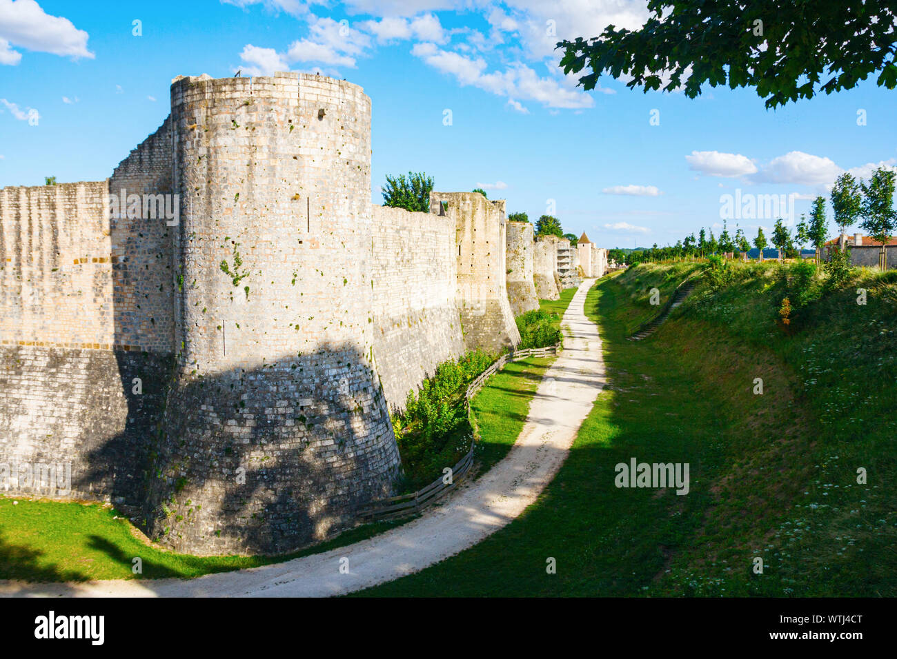 Mura medievali della città rinforzata con una massiccia torre rotonda e da un profondo fossato sotto un cielo blu con nuvole in una giornata di sole. Provins, Seine-et-Marne, Francia. Foto Stock