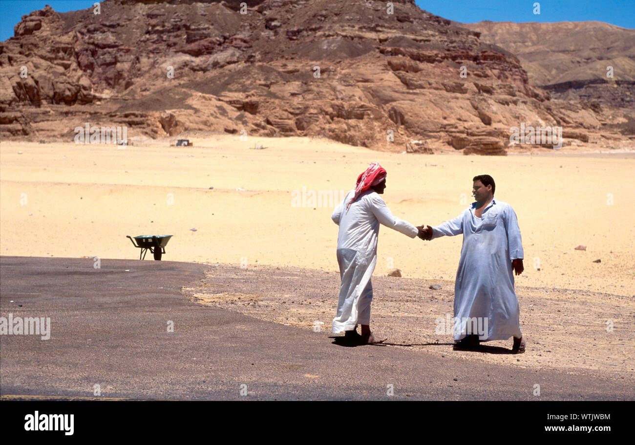 Due uomini stringono le mani nel deserto. Foto Stock