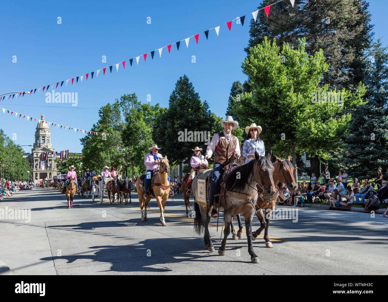 Montato (e buckboard-riding) cowboy e cowgirls corsa giù Capitol Avenue in uno dei numerosi cortei durante l annuale Cheyenne Frontier Days celebrazione in città con lo stesso nome. Il Wyoming Capitol è visibile dietro i piloti Foto Stock