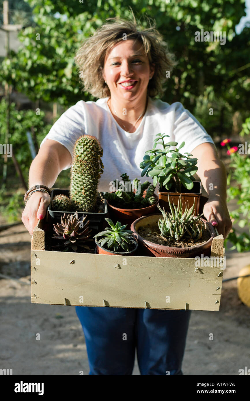 Giovane donna sorrisi come lei si mette in mostra la sua captus e piante su un soleggiato d Foto Stock