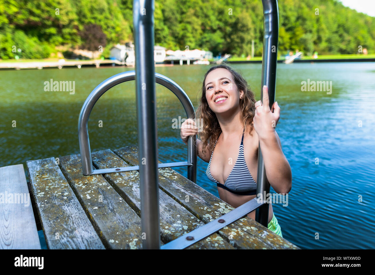 Ricci bella donna che indossa un bikini sulla scaletta per uscire da un lago sulla giornata di sole. Vacanze Estate concetto. Foto Stock