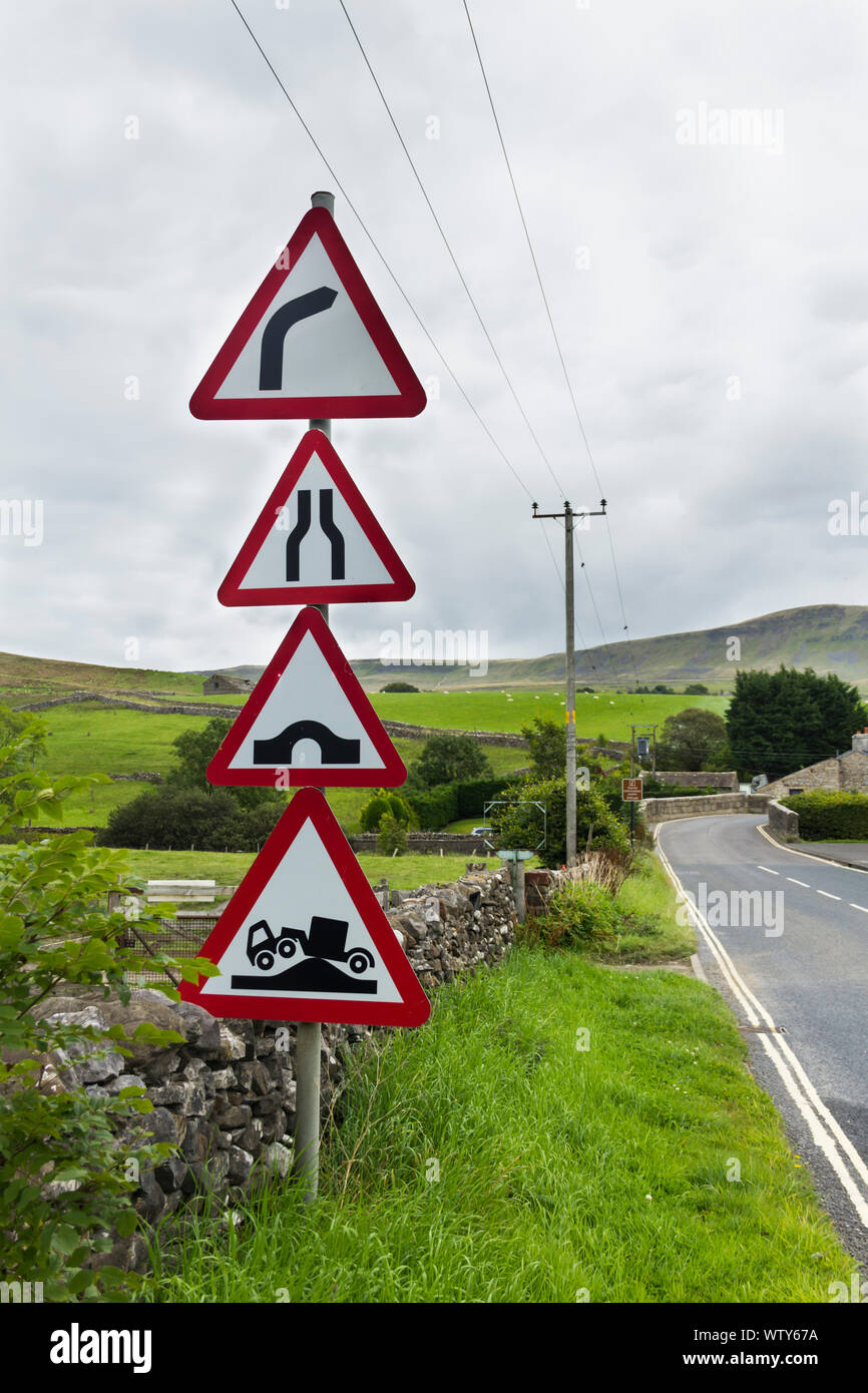 Più cartelli di avvertimento sulla strada di avvicinamento di una curva a gomito e humpback ponte sulla B6479 nel villaggio di Horton in Ribblesdale, North Yorkshire. Foto Stock