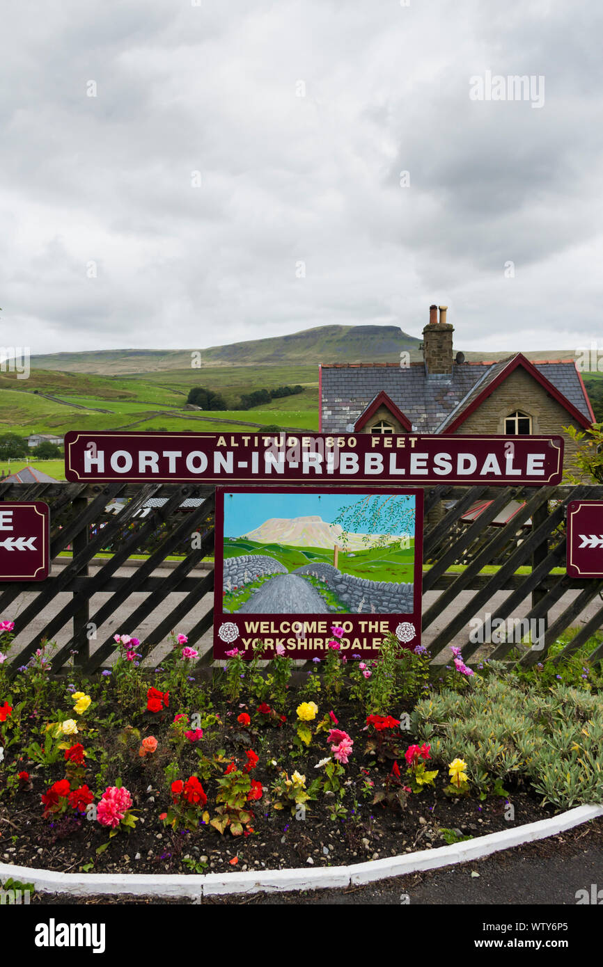 Aiuola e segno della stazione sulla stazione ferroviaria a Horton in Ribblesdale, North Yorkshire dominato da distante Pen-y-Ghent. Foto Stock