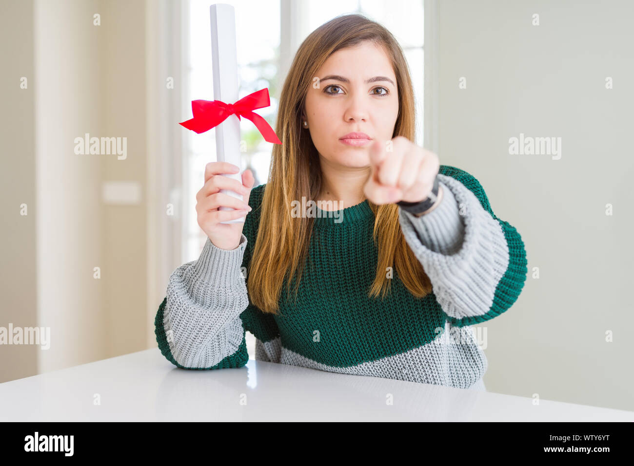 Bella giovane donna grado di contenimento con fiocco rosso puntando con il dito per la telecamera e a voi, mano segno, positivo e fiducioso gesto dal p. Foto Stock