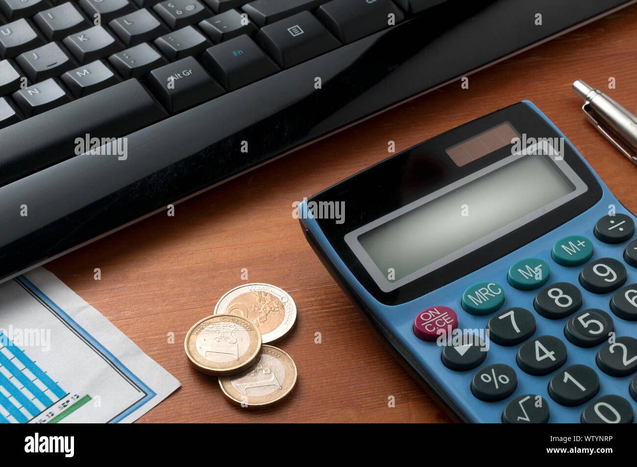 Calcolatrice sul tavolo di legno con una penna e alcune monete in euro nella parte anteriore di un nero della tastiera del computer Foto Stock