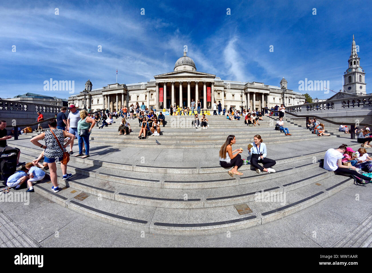 Londra, Inghilterra, Regno Unito. Trafalgar Square - la gente seduta sui gradini davanti alla Galleria Nazionale Foto Stock